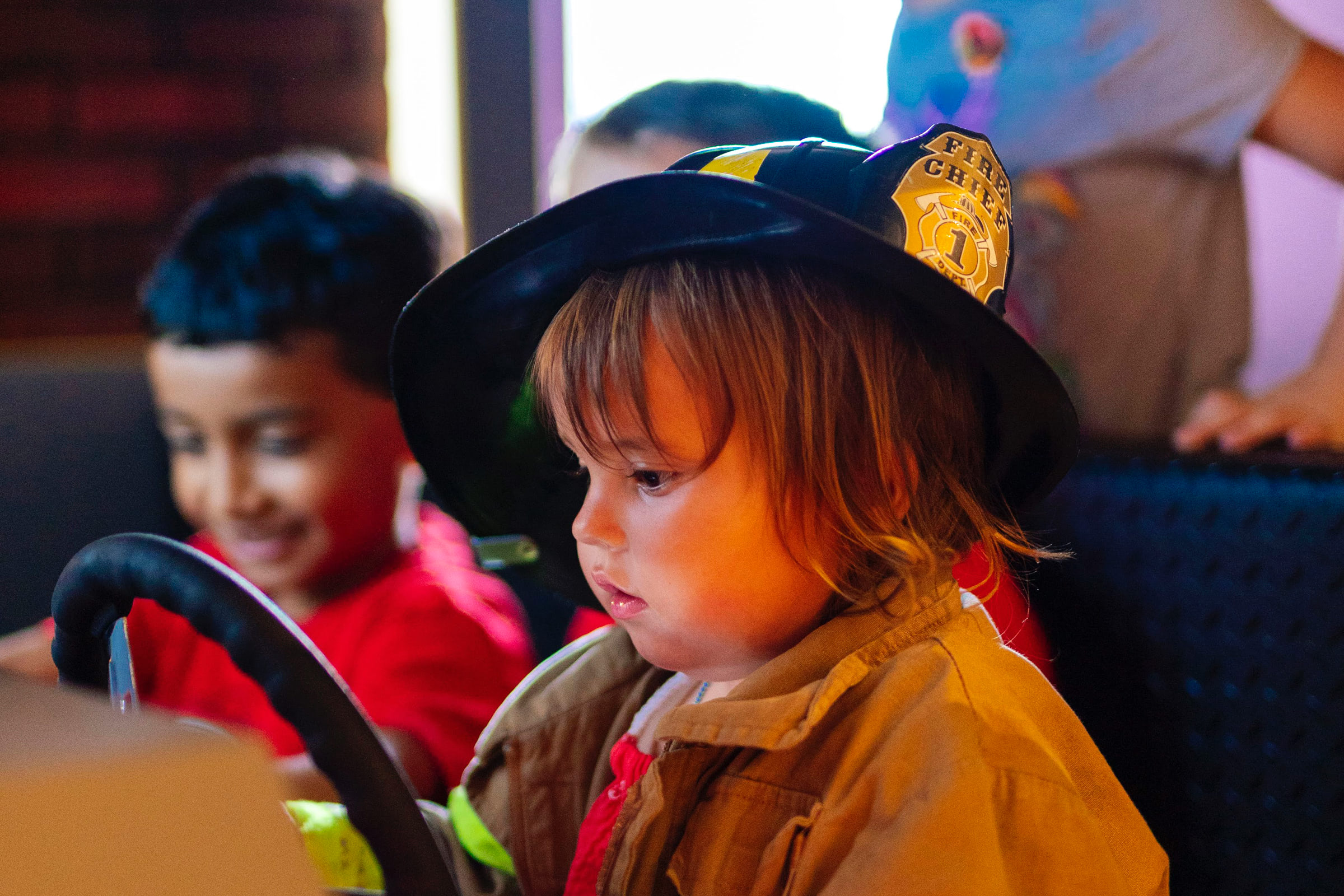 Children in a pretend fire truck wearing a firefighter hat
