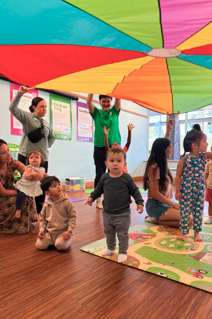 kids playing under a colorful parachute held by adults