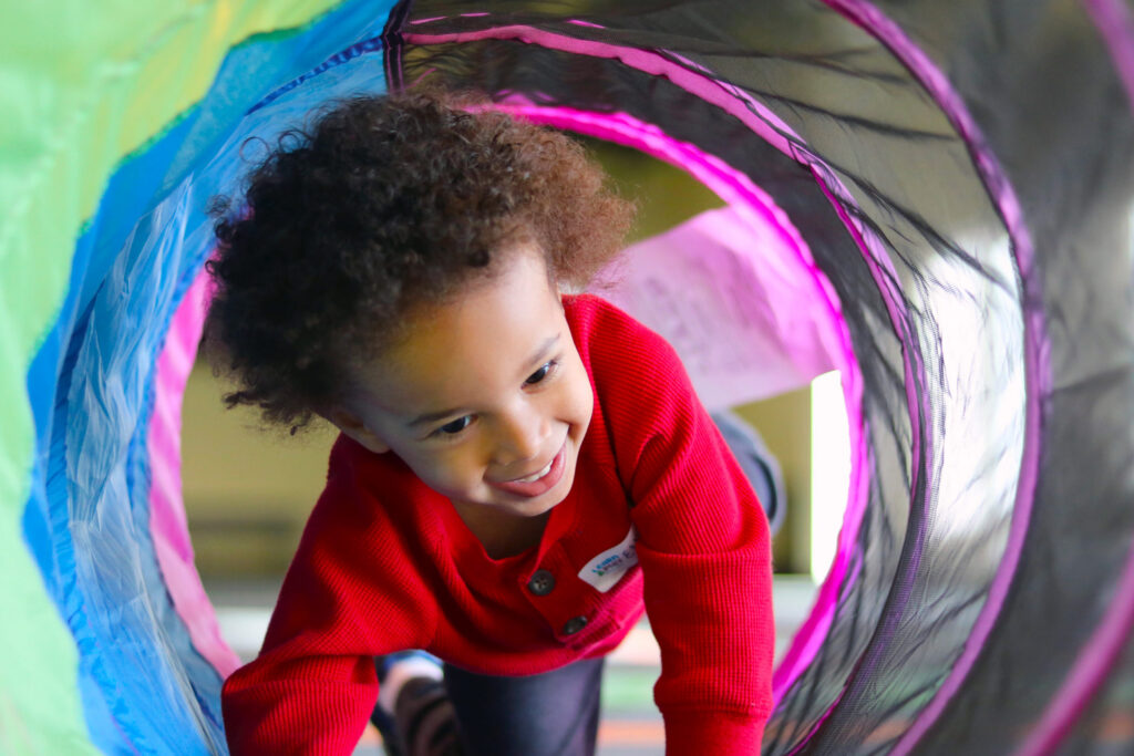 Child smiling and crawling through a tunnel