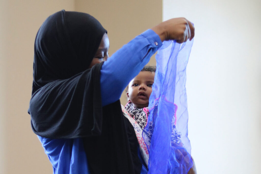 parent holding a baby and playing with a scarf