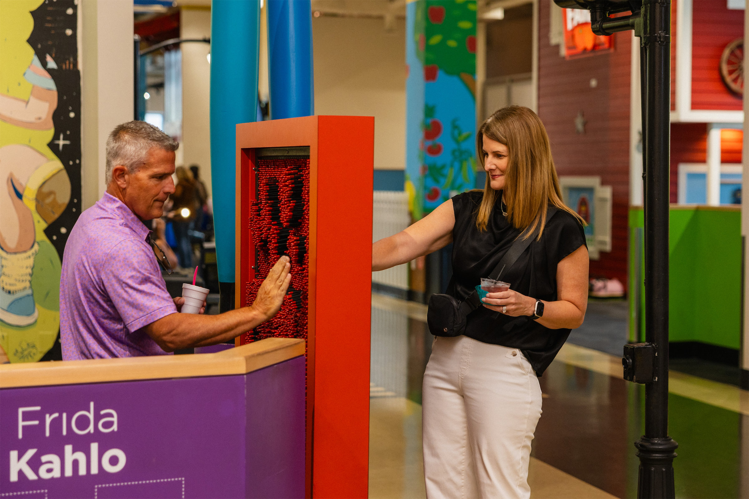 A Man and a woman with drinks playing at the Frida Kahlo section of the Glazer Children's Museum